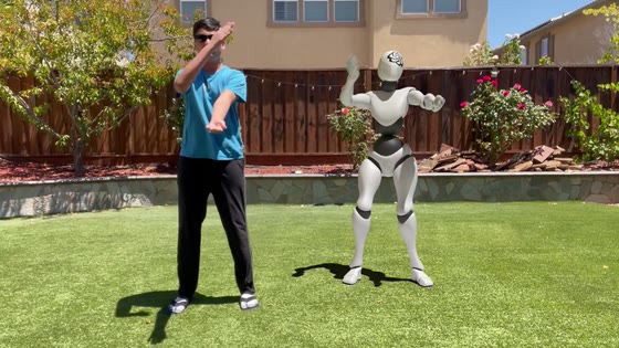 Pransh dancing in a backyard next to a white animated robot that copies his moves.